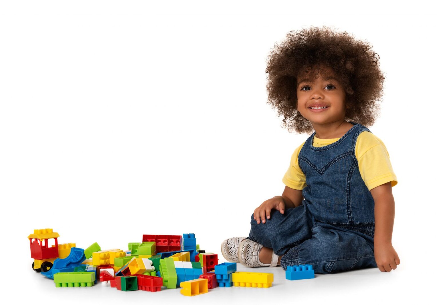 Lovely little cute african american girl playing on the floor with lots of colorful plastic blocks in studio, isolated on white background